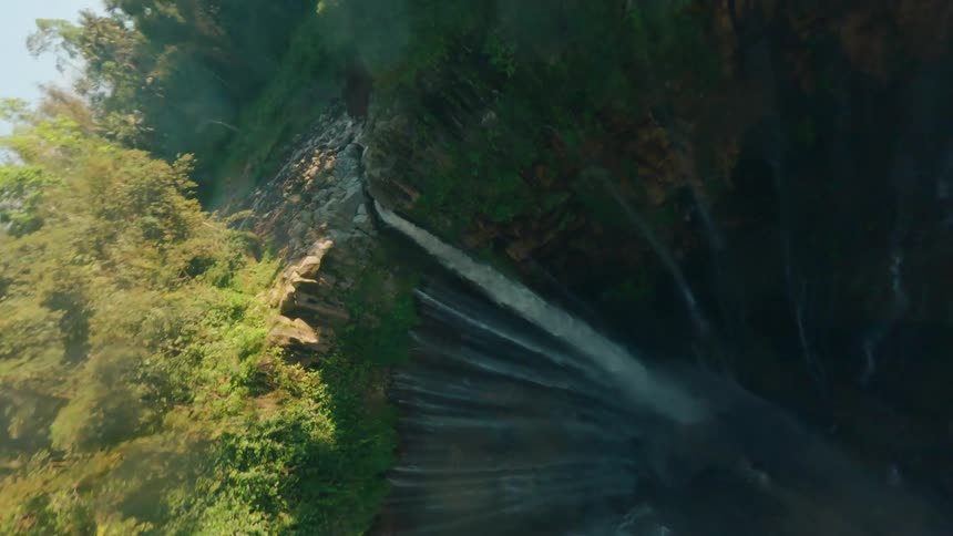 FPV drone clip of a waterfall plunging from a cliff surrounded by lush forest