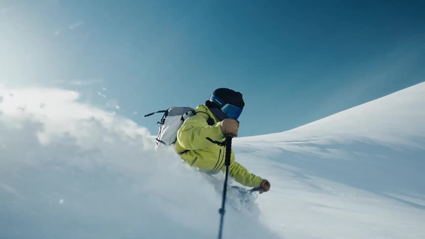 A skier glides down a snowy mountain slope under a clear blue sky