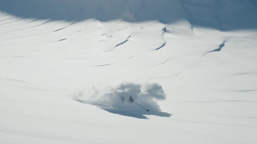 Skier descends a slope covered in fresh snow under bright light