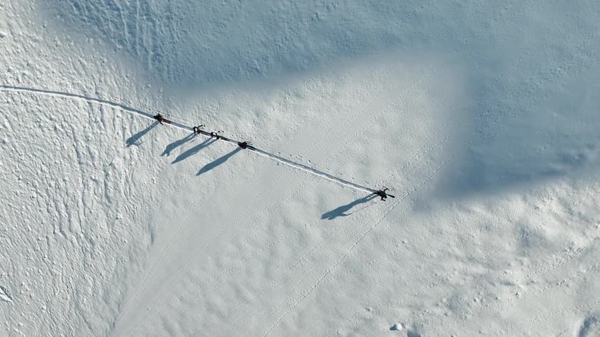 A group of people is cross country skiing across a wide area of snow