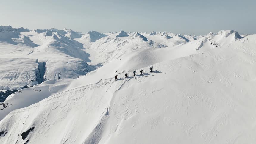 A group of hikers crosses a snowy mountain ridge amid a vast winter range