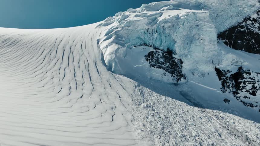 Snowy slope with crevasses and ice formation under deep blue sky