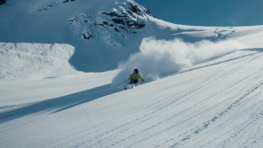 A skier glides down a sunlit snow covered mountain leaving winding tracks behind