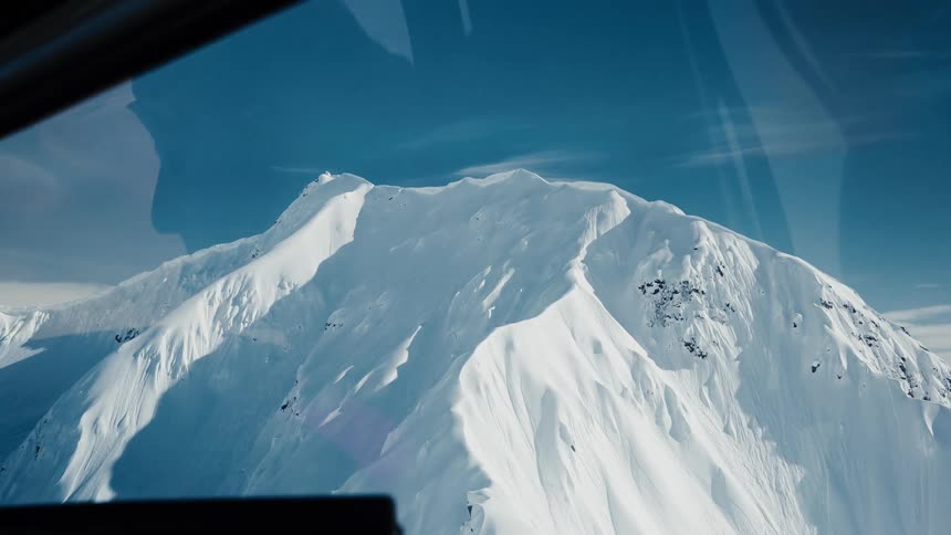 Snowcovered peak seen from inside an aircraft under a clear blue sky