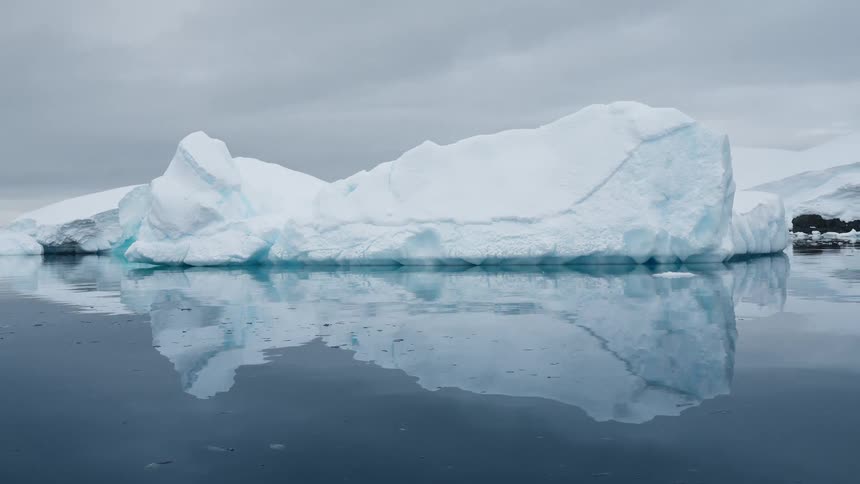 A large blue iceberg floats in dark ocean water beneath an overcast sky