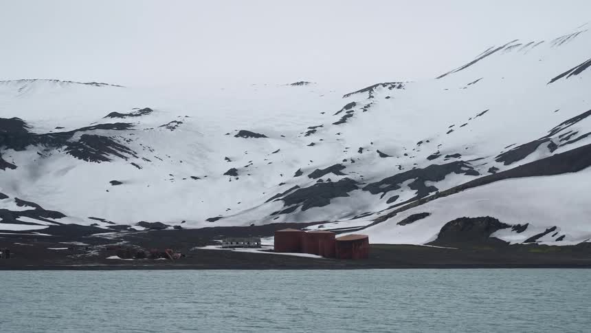 Rusty tanks stand by the sea in front of snowcovered mountains