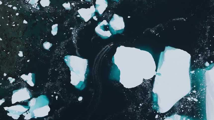 Ice blocks float in dark sea with a boat passing between them