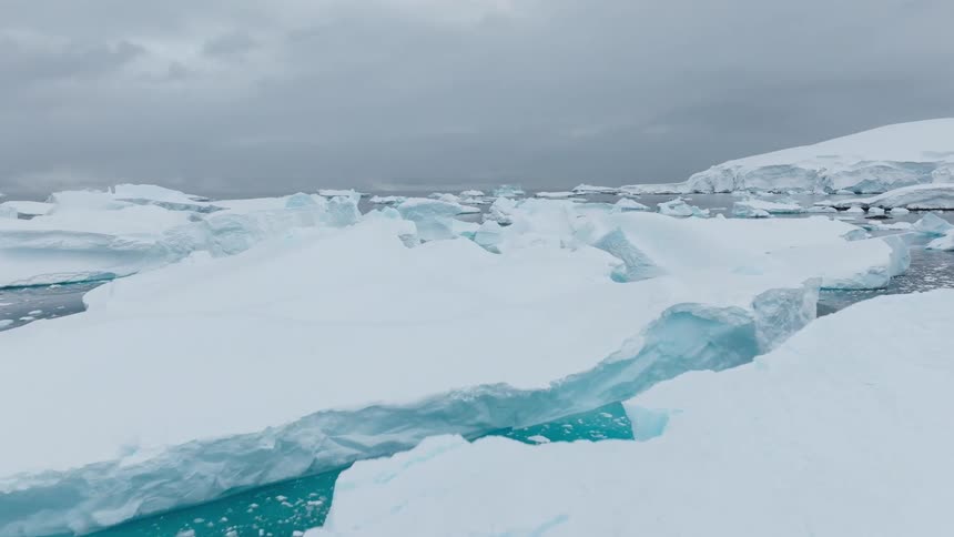 Bluish ice formations float in polar sea under cloudy sky