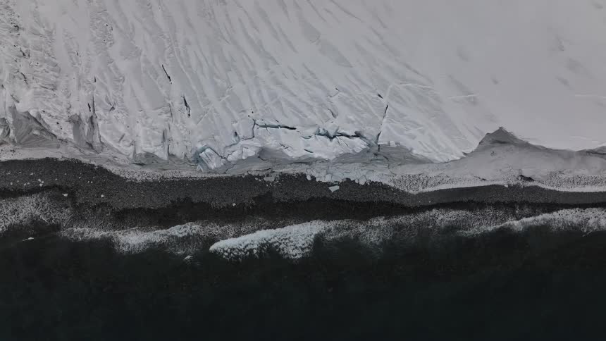 Edge of ice meets dark strip of rocks and cold sea