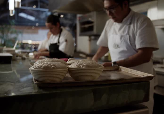 Male baker in the kitchen greases a tray while prepping bowls of dough