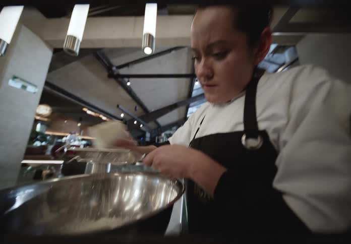 A woman grating cheese into a bowl in a kitchen