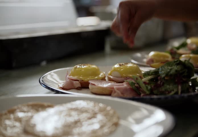 Finishing touch being added to eggs benedict with salad on the side