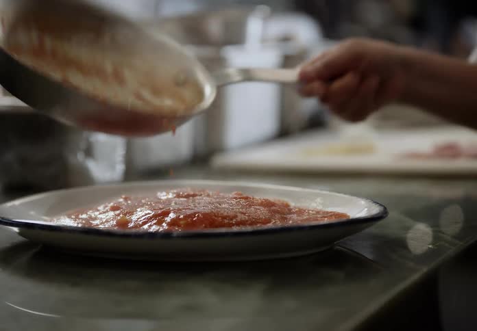 A persons hand pouring red sauce from a pan onto a white plate