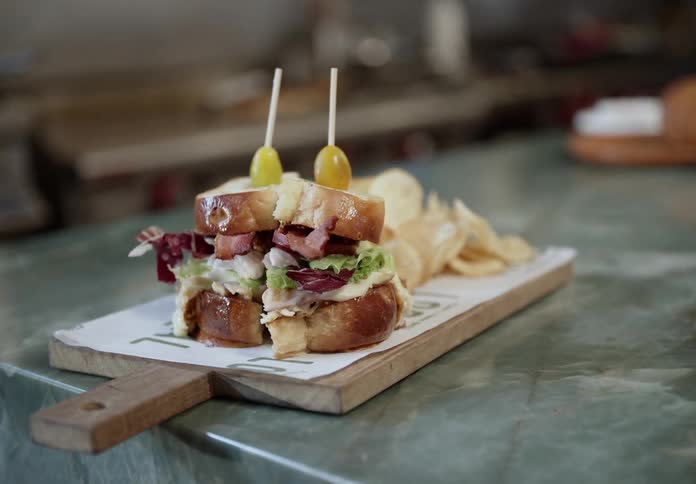 Gourmet sandwich with bacon and lettuce served on a board with chips