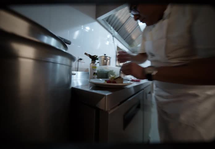 In a long professional kitchen a chef meticulously plates a dessert with fresh berries as the camera moves in for a close up of the final arrangement