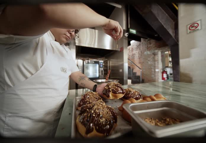 Man spread chopped nuts onto a chocolate topped dessert while working in a commercial kitchen
