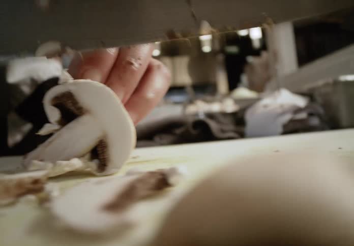 Slice of mushroom being cut with a knife on a cutting board