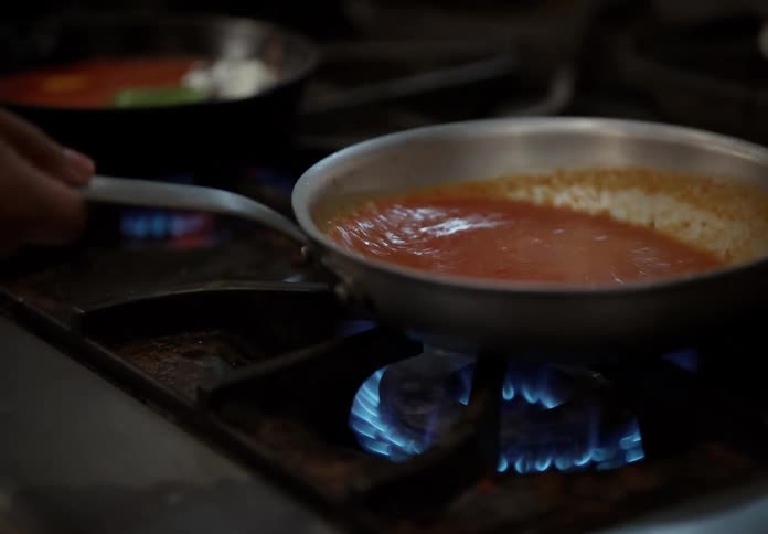 Cook jiggles a skillet over a lit burner while cooking a sauce