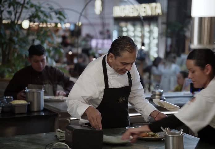 Workers in a restaurant serve food to a customer at the bar