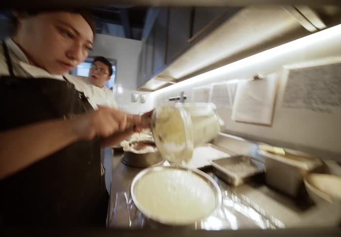 Cooks preparing desserts on a brightly lit kitchen counter