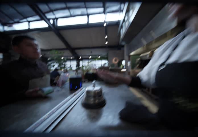 Woman working behind a restaurant counter rings a bell and speaks to a customer
