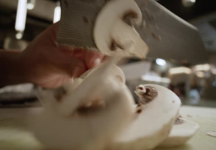 A persons hand holding a knife cutting a white vegetable into several slices