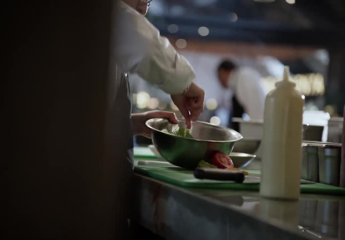 Chef adds dressing to the salad in a bowl mixing the items together