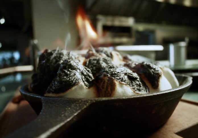 A person using a blowtorch to burn the surface of food in a pan