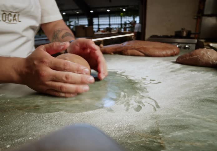 Baker kneads dough on a floured counter in a bakery setting