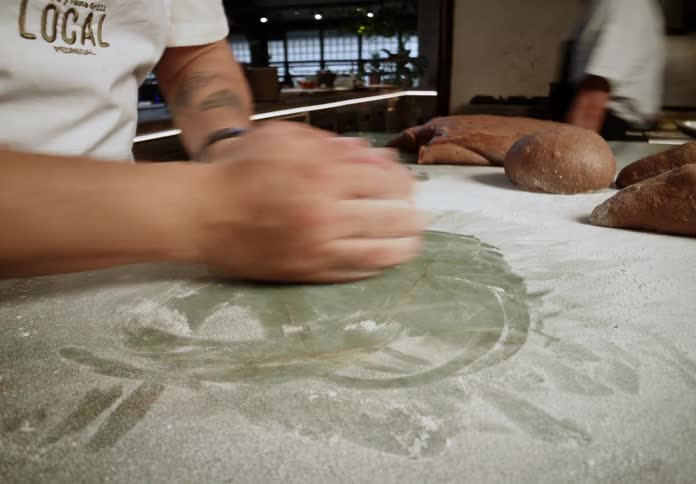 A man rolls a piece of dough on a counter top covered in flour