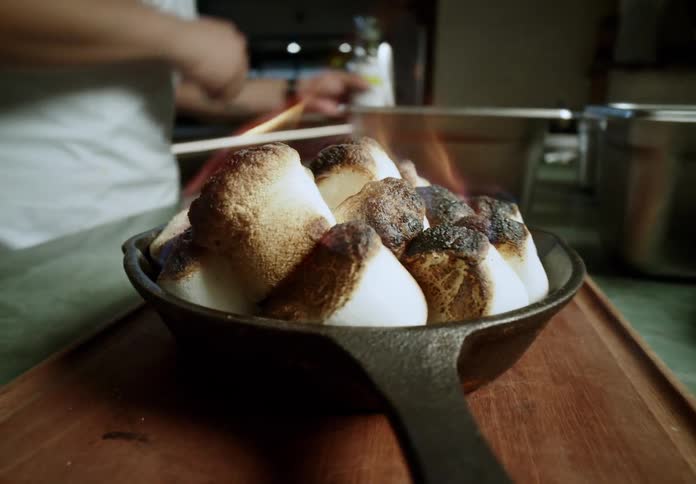 Cook toasting marshmallows with a torch in a castiron skillet