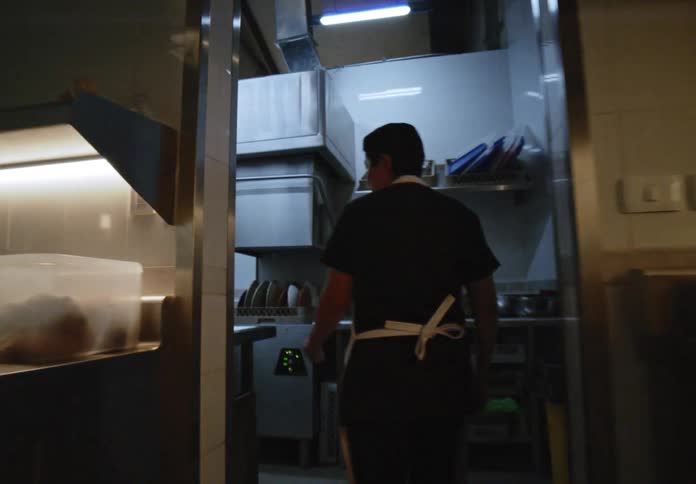 Man walks through a commercial kitchen and pulls down the cover on a commercial dishwashing machine