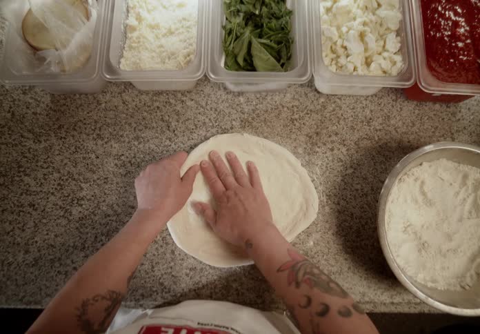 Pizzaiolo shaping pizza dough surrounded by fresh ingredients