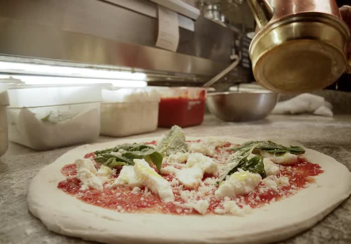 In a professional kitchen a chef drizzles olive oil onto a freshly prepared margherita pizza topped with tomato sauce mozzarella and basil