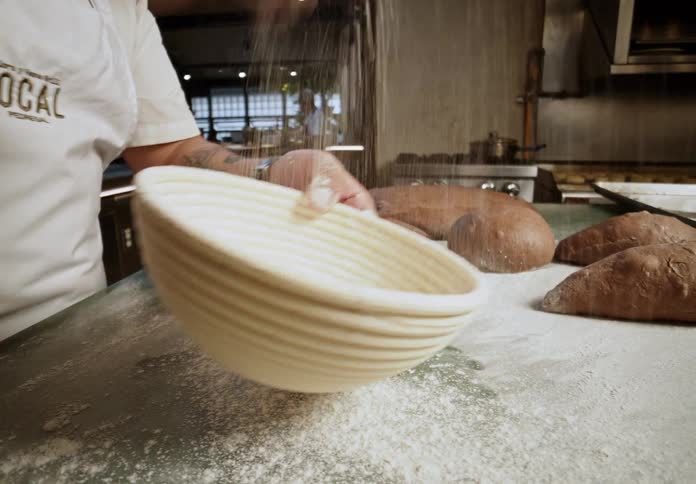A male cook in a restaurant kitchen sprinkles dough with flour and places it in a floured bowl