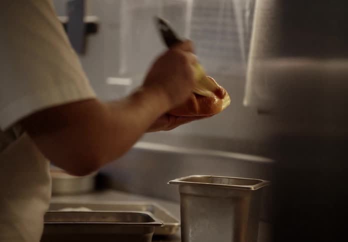 In a professional kitchen a chef carefully brushes a glaze onto a freshly baked bread roll