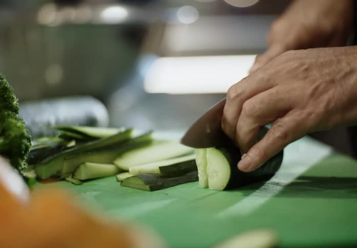 An adult slices cucumbers with a large butcher knife