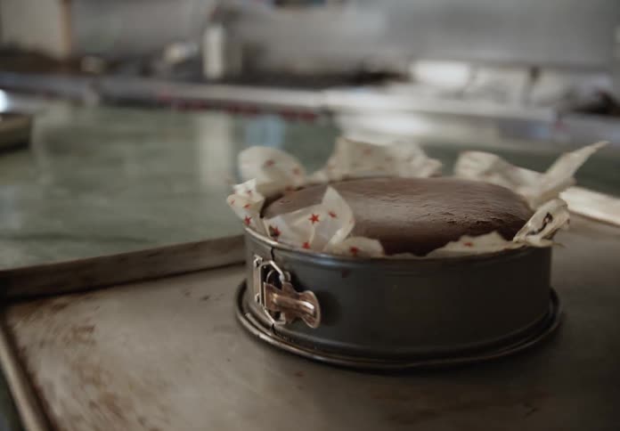Male dessert maker pulls a cheesecake from the oven and puts it onto a rolling shelf