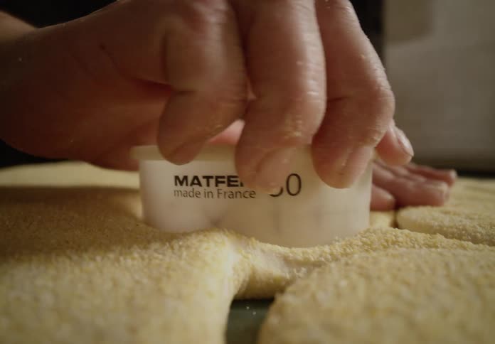 A persons hands are shown using a plastic cutter pressing into dough to make round shapes