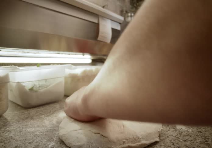 In a restaurant kitchen a chef sprinkles flour onto a countertop and expertly kneads a ball of fresh dough