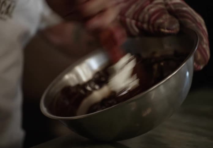 A person uses a spatula to stir a chocolate mixture in a bowl