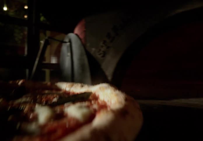 Pizza is slid into a fire burning oven briefly before being placed on a circular board in a commercial restaurant in the evening