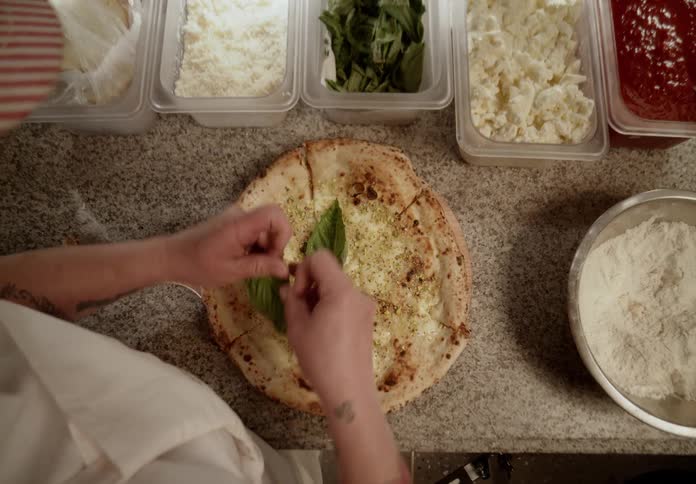 A woman chef is putting fresh basil on top of a cooked pizza
