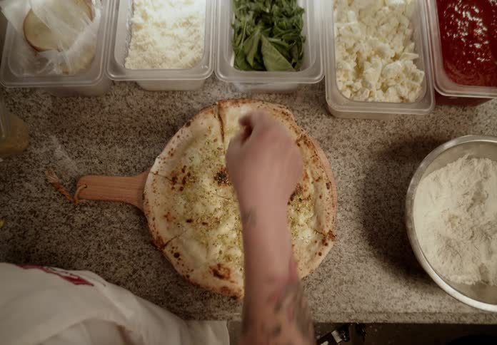 Chef adds ingredients to a pizza crust while working in a commercial kitchen