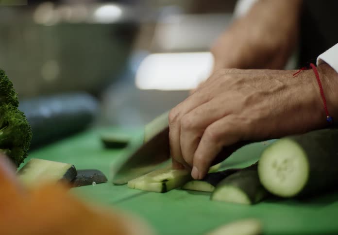 A chef carefully slices a fresh cucumber on a green cutting board