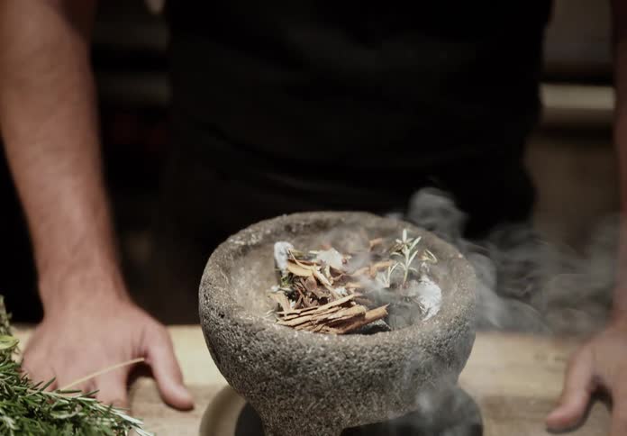 Chef adds spices to a stone mortar with burning herbs and twigs