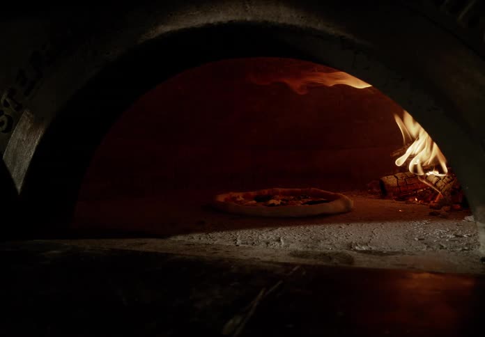 A fresh pizza on a peel is placed into a woodfired oven