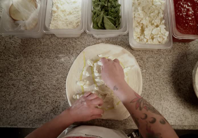 A person is carefully making food preparation i think it is pizza cheese and other toppings are being added to it