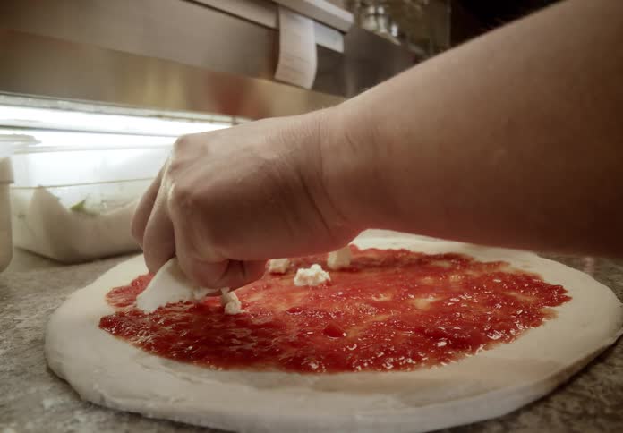 A man makes a fresh pizza with marinara sauce and mozzarella cheese