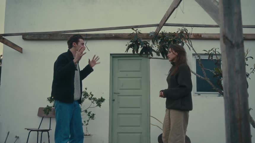 Man and woman talking tensely in front of a modest house